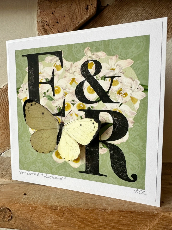 A mint green wedding, monogram card, showing the initials E and R. The initials are black and placed on a white orchid heart. A white 3D hand cut paper butterfly sits on the bottom left of the heart. The card has the option to personalise further with the names of the couple, handwritten and the wedding date in the bottom, border of the card.