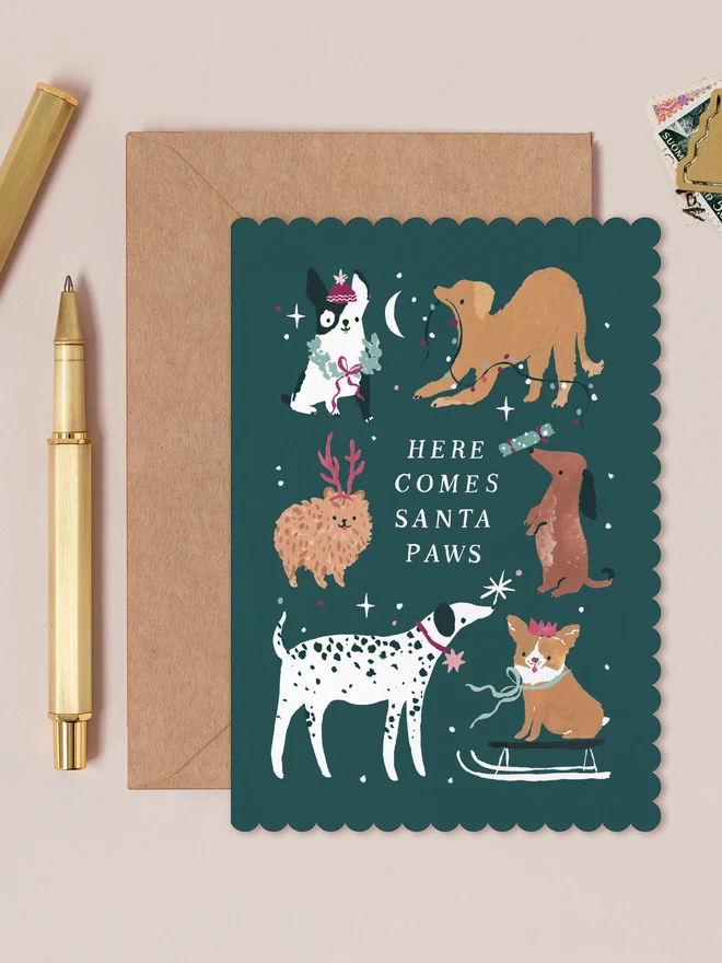 Santa Paws Dogs Christmas Card by Sister Paper Co, six illustrated dogs enjoying the festivities on a dark teal background with the caption Here Comes Santa Paws