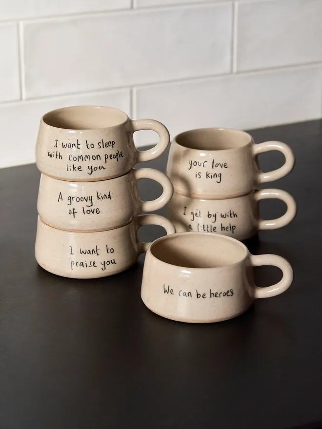 a full set of cream ceramic mugs with a range of phrases