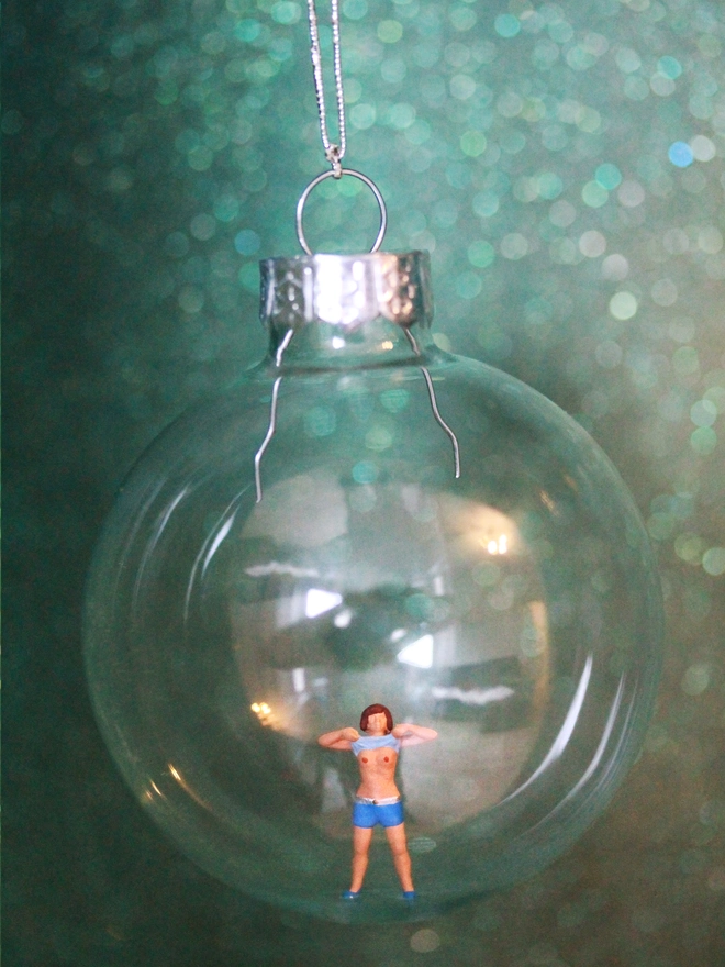 Miniature figure of a female playfully flashing her boobs in a glass Christmas bauble 