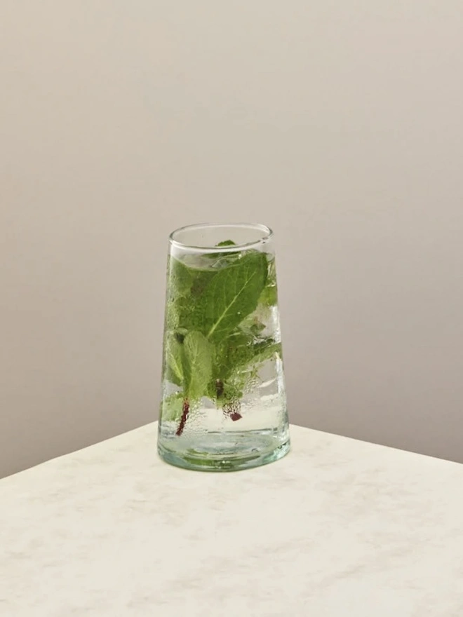 Highball Glasses (Set Of 1 Or 4), a highball glass sitting on a plain counter top against a white backdrop. It is filled with a soft drink. 