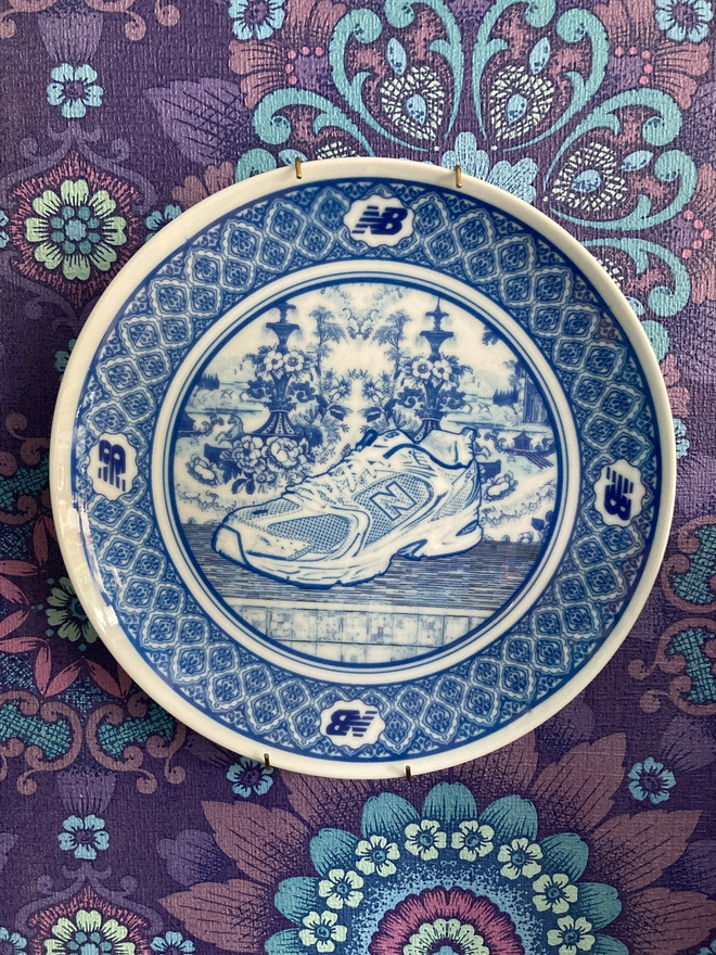 blue and white Delft style ornamental plate featuring an illustration of a New Balance trainer in the center.