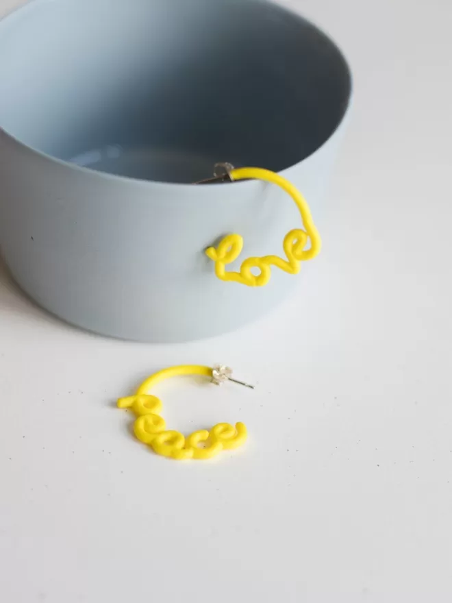 Love and Peace Yellow small earrings seen in a blue cup.