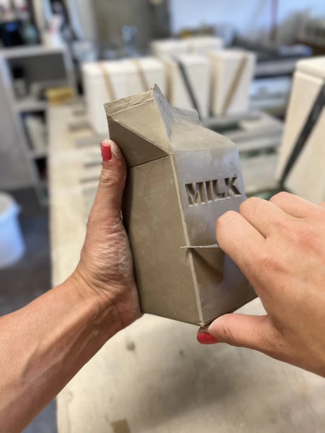 Katie is trimming the seam, left by the casting process, on a freshly made clay milk carton.
