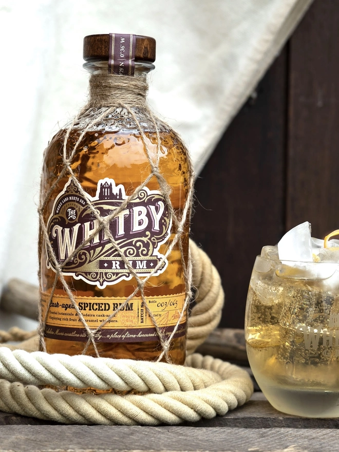 Whitby Rum, a bottle of rum sitting on a wooden surface joined by a rope. 