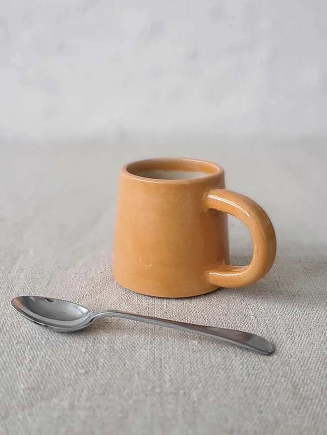 Classic Ceramic Espresso Mug, a colourful ceramic espresso mug sitting on a plain surface against a white backdrop. It is accompanied by a spoon. 