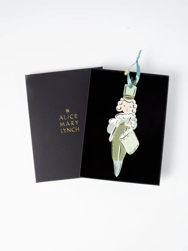 Little Drummer Tree Dancer. wooden hanging little drummer decoration in an open black gift box embossed "alice mary lynch" in gold, with a curly white wig, sage green hat, uniform and drum, duck egg blue ribbon with a jingle bell
