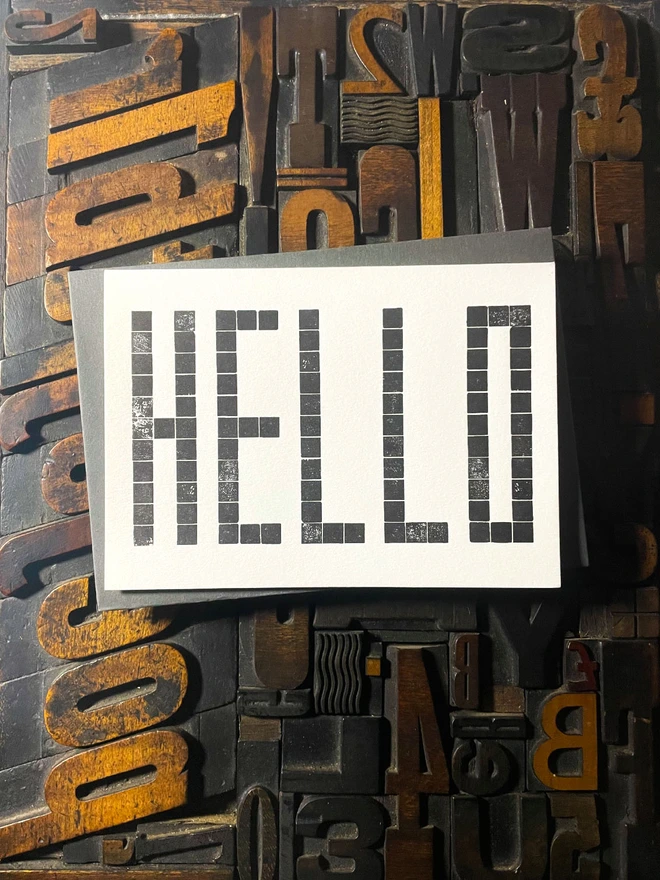 Letterpress HELLO postcard printed from a grid of square wooden type blocks in rich black ink, deeply impressed on thick 350gsm Colorplan Pristine White card.