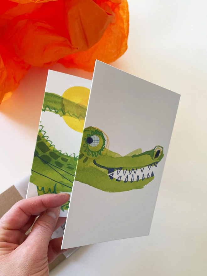 Esther Kent illustrated concertina greeting card showing a creen crocodile on a white background, with colourful balloons