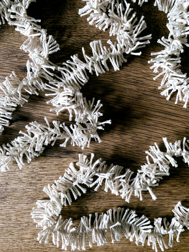 A squiggle of white Plain Cotton Strinsel (plastic free string tinsel) on an oak background
