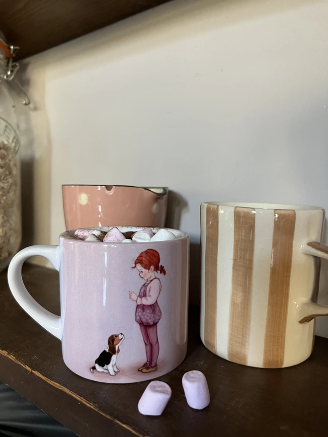 a small childs ceramic mug featuring a story book style illustration of a little read haired girl teaching her Beagle puppy to sit pink and lilac in colour