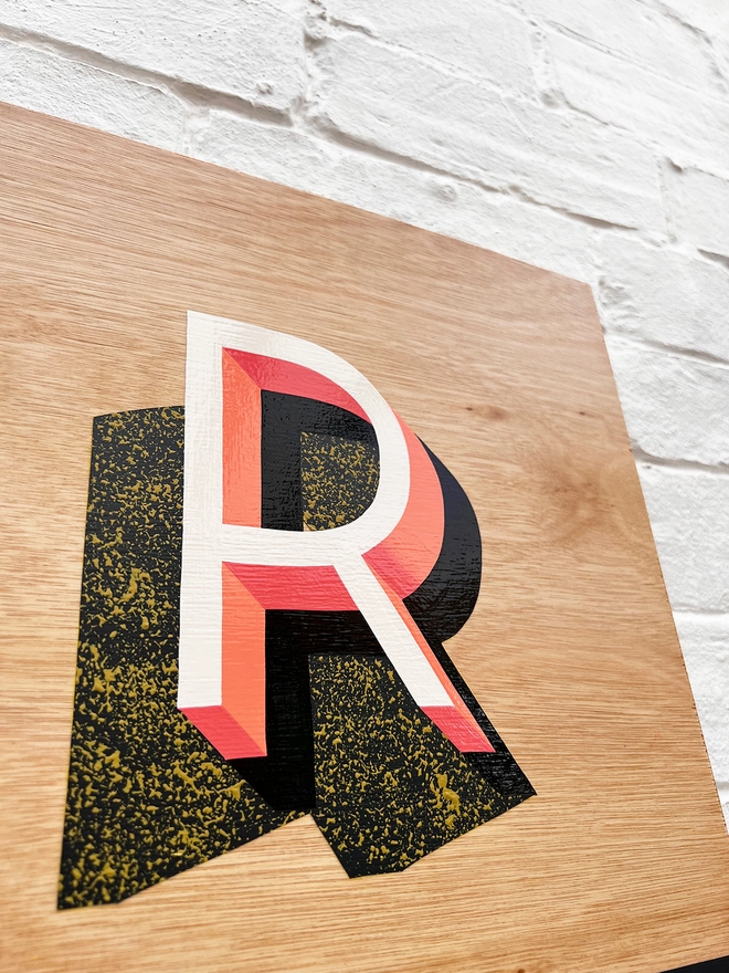 Close up of letter R from GROW hand painted sign in coral, dark grey and chartreuse, against a white brick wall, at an angle. 