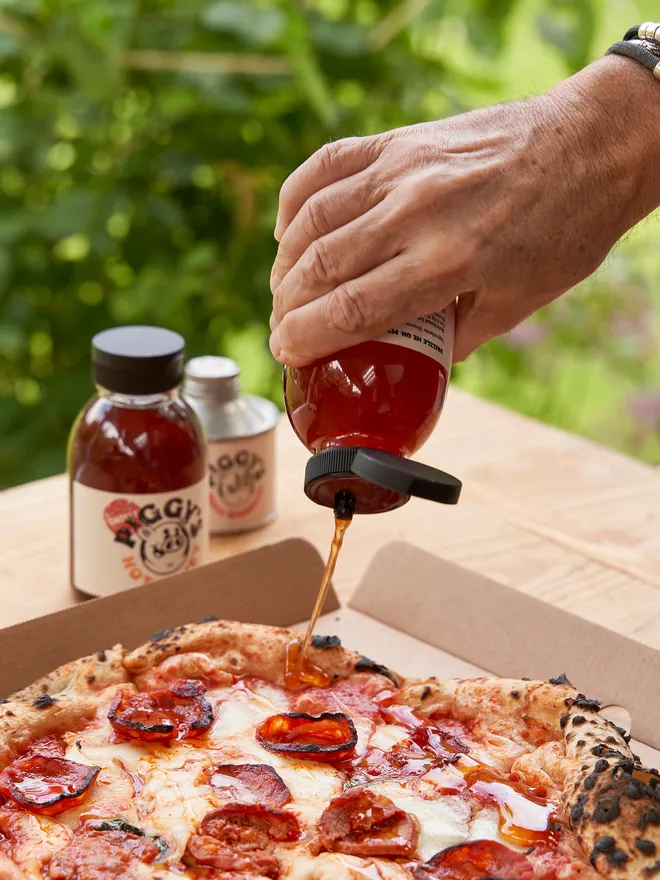 Piggy's Hot Honey- held up against a pizza in the garden 