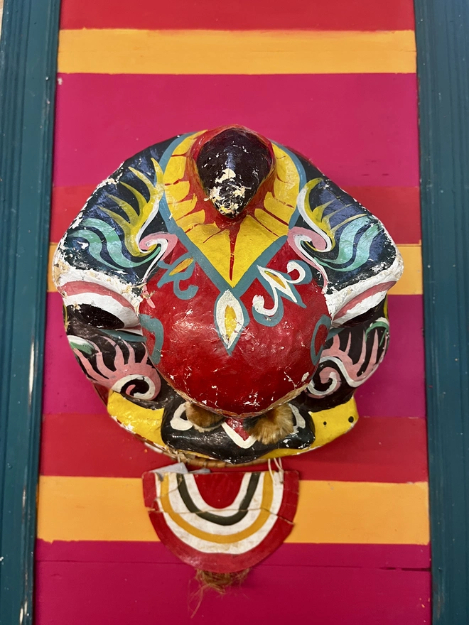 welcome to the circus sign, with colourful stripes of pink, yellow and orange with a teal frame and zig zag pattern at the top and the bottom. surrounded by a teal frame. with a vintage mask from Thailand which inspired the colour palette