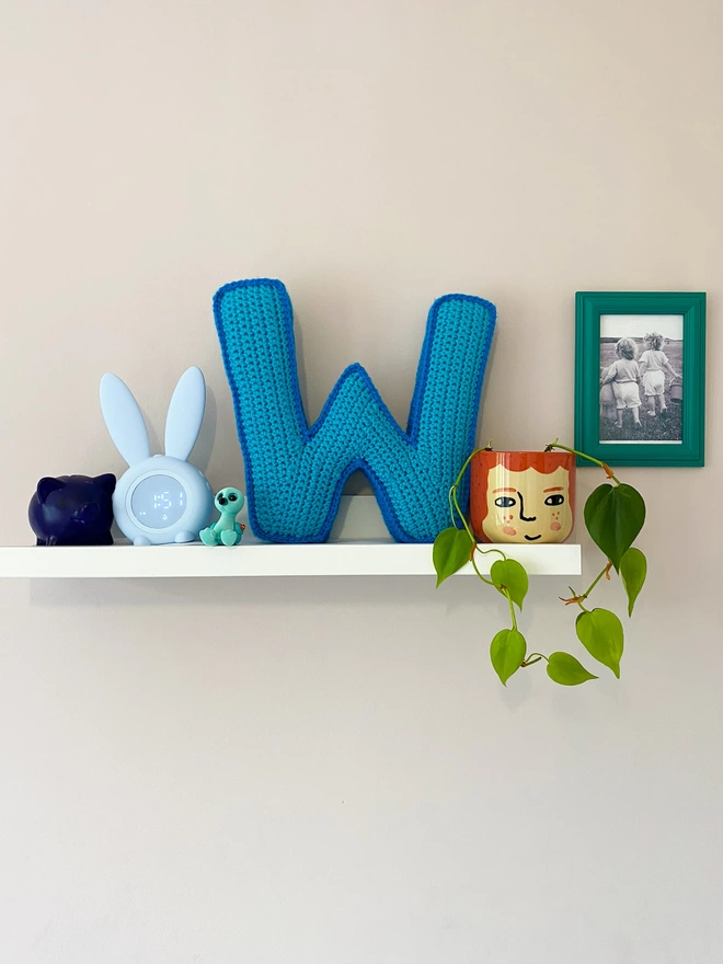 Crocheted W Cushion in Light Blue and Blue, on a shelf