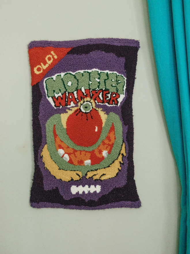 'Monster Wanker' Handmade Tufted Rug/Wall Hanging seen hanging on the wall next to a teal curtain.