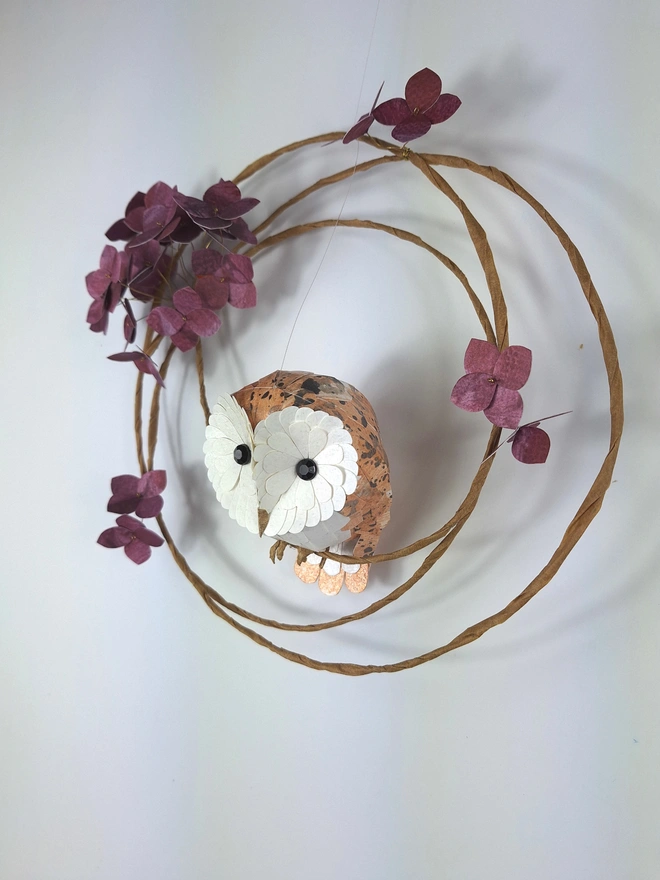 handmade paper sculpture of a baby barn owl, perched on a floral wreath of mulberry hydrangea