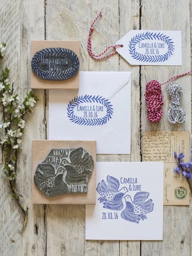 Wooden lino cut rubber stamp with two illustrated love birds and the text ‘Camilla & Luke’ and the date ‘28.08.16’, shown next to a blue ink stamp impression on white paper.