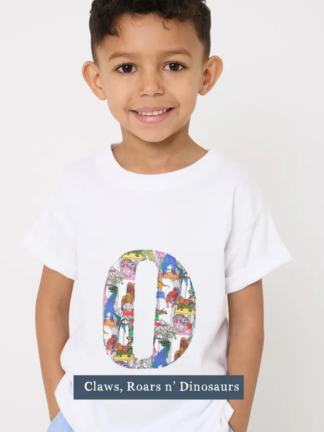 a 4 year old boy wearing a personalised kids white t-shirt with an initial cut from liberty dinosaur print on the front