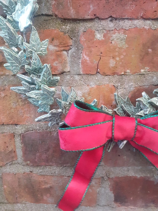 Close-up of textured ceramic ivy leaves with verdigris glaze and metallic copper highlights beside a red velvet ribbon edged in shimmering green.