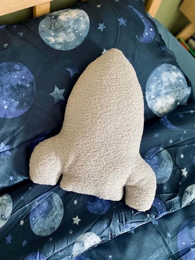 boucle rocket pillow. aa grey rocket cushion on a bed with space-themed sheets.