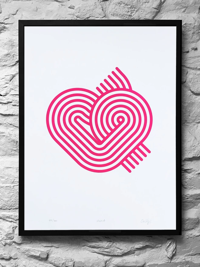 A black framed print hung on a rough whitewashed wall, with a magenta contemporary stirpy heart design on a big piece of white