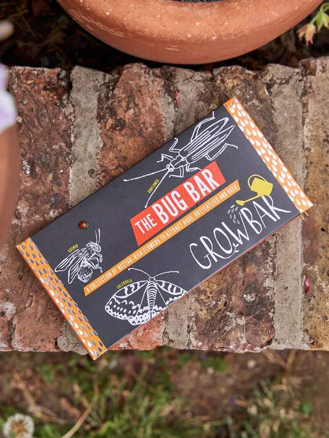 The Kids Bug Growbar - placed outside on a brick wall awith plants soil and grass in the shot 