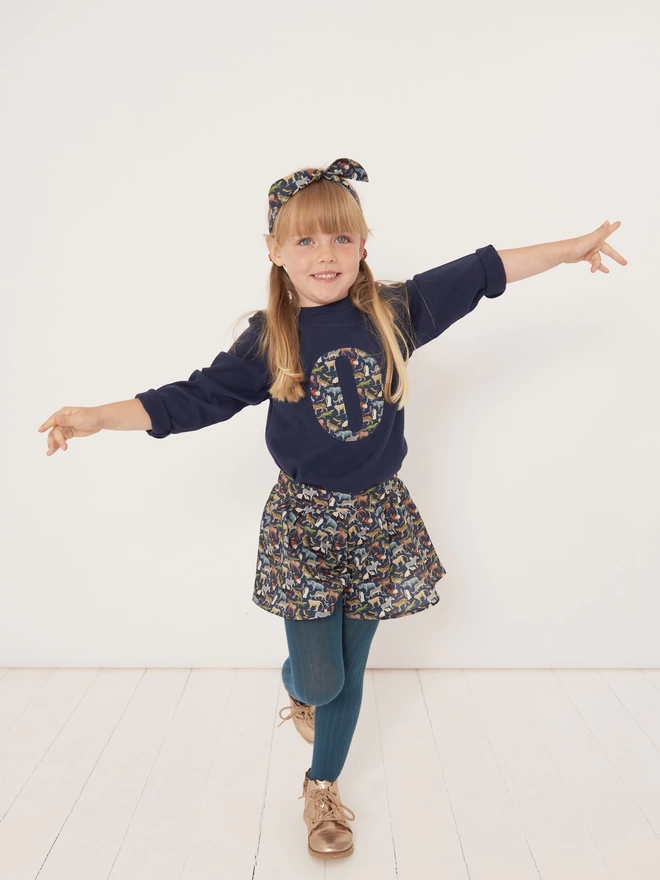 girl wearing a navy long sleeve tee with her initial on in Quey 2 Liberty print