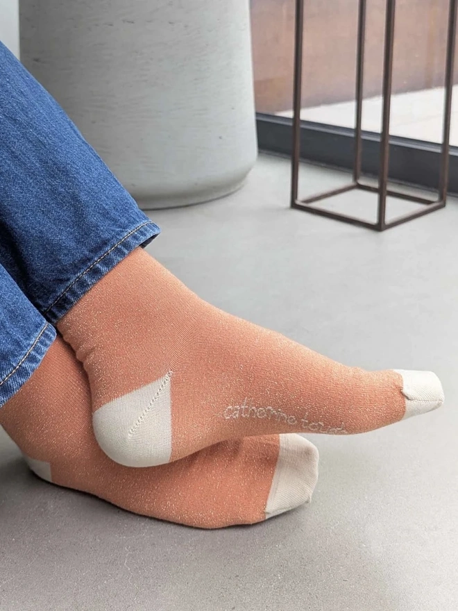Women's Glitter Organic Cotten Ankle Socks, a woman wearing a pair of colourful patterned socks above a decorated surface. 