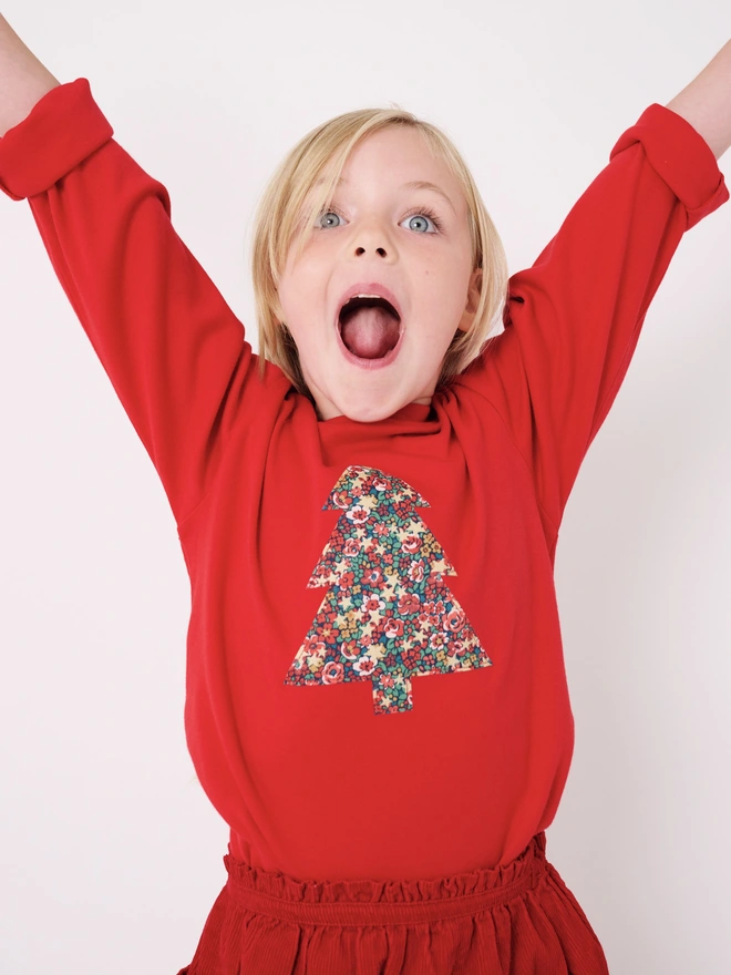 a happy 4 year old wearing a red t-shirt with a christmas tree cut from liberty floral fabric sewn onto the front