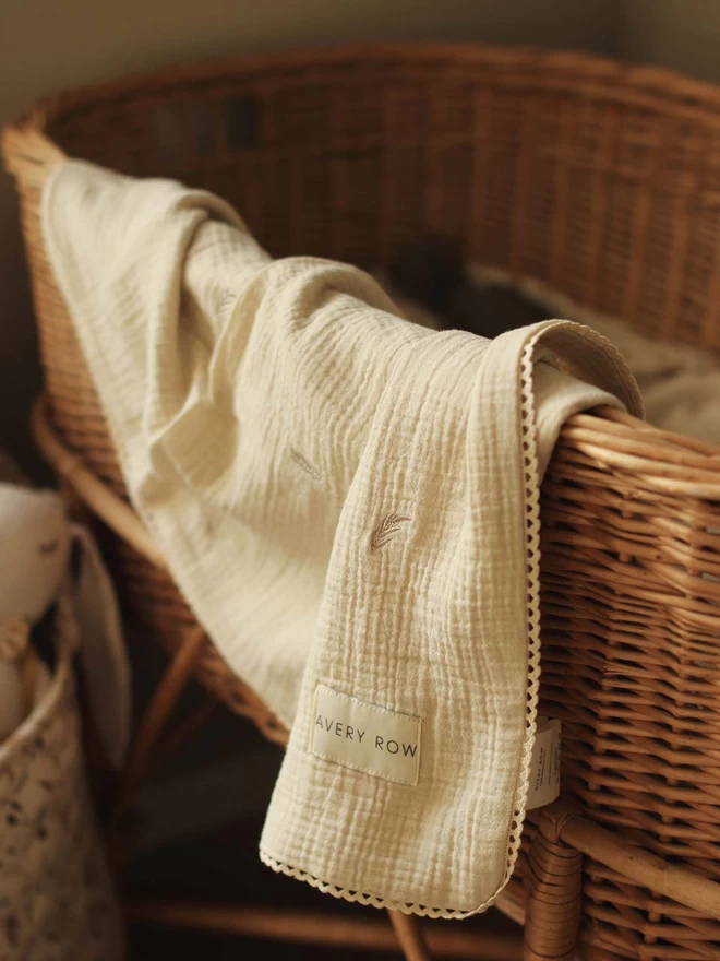 An embroidered muslin blanket grasslands folded on a baby changing basket