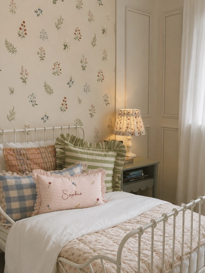 Personalised pink striped stonewashed linen cushion with ruffle trim, hand-painted ditsy florals and embroidered name, styled in a floral children’s bedroom.