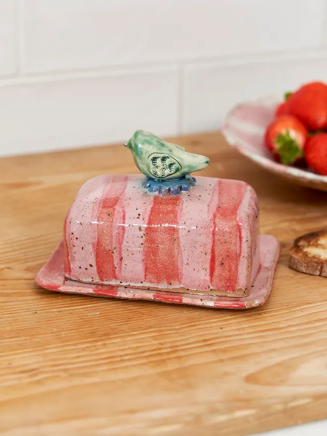 Bird pink and red striped butter dish on a wood surface 