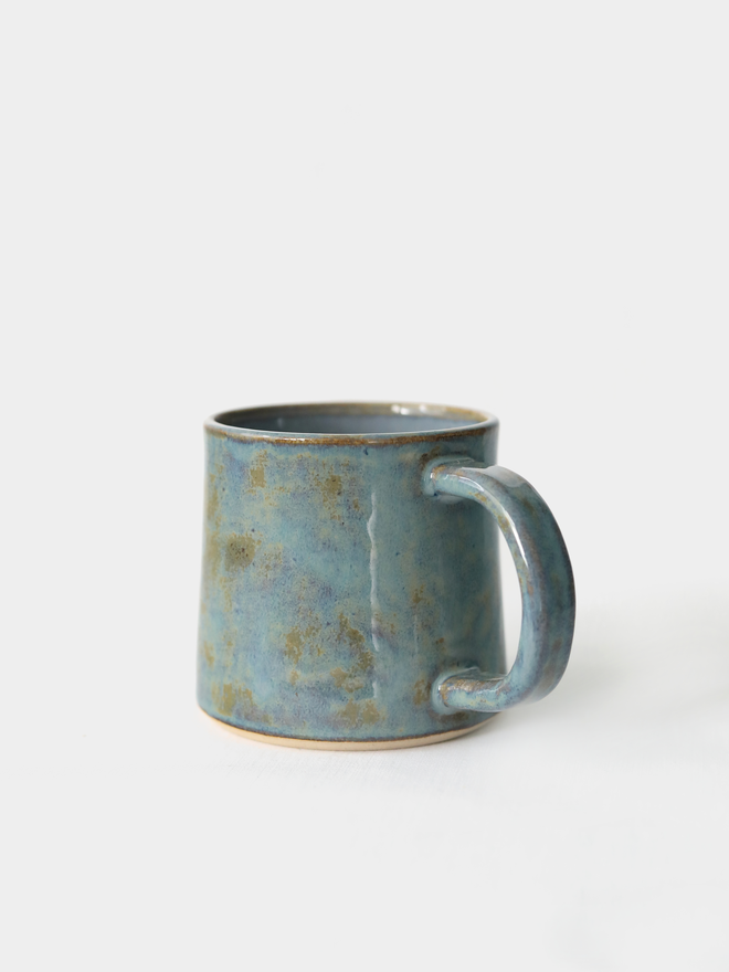 A handmade ceramic standard mug in glossy seafoam blue glaze with a chunky loop handle, photographed against a plain light grey background