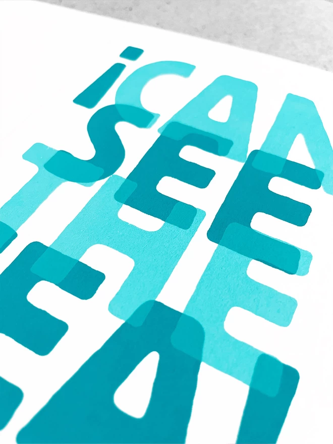 close up of the overlapped turquoise screenpritned words saying I Can See the Sea.