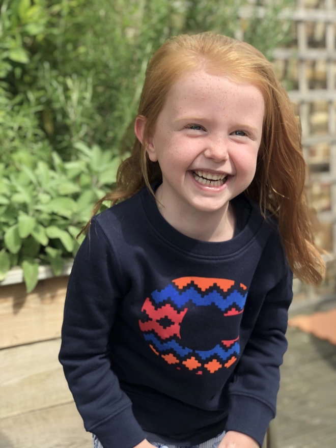 a little girl is laughing and wearing a 'Narrator' Sweatshirt by The Faraway Gang in Navy.
