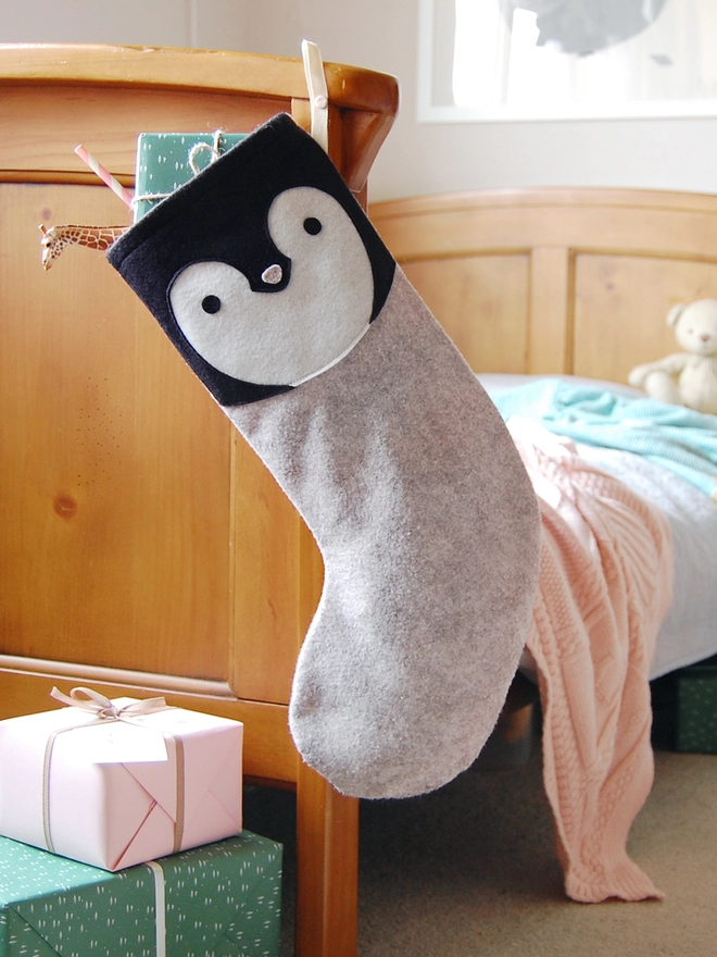 A handmade felt penguin stocking hangs on the end of a wooden bed.
