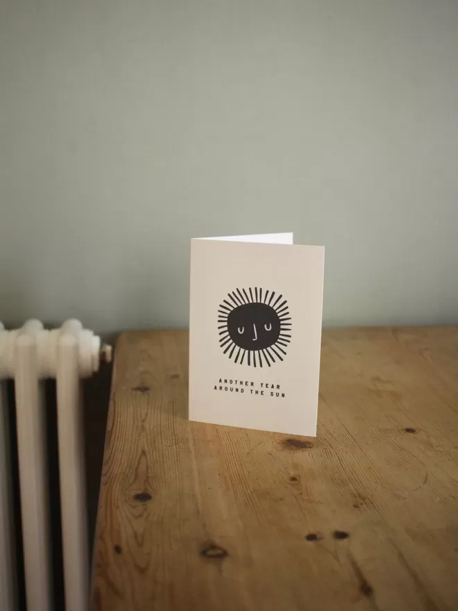 Black and white birthday card with illustration and the words Another year around the sun written on it stood up on wooden table