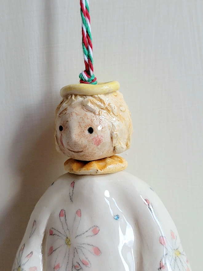 close up of the face of an angel pottery decoration with blonde hair, halo collar and daisies on her dress