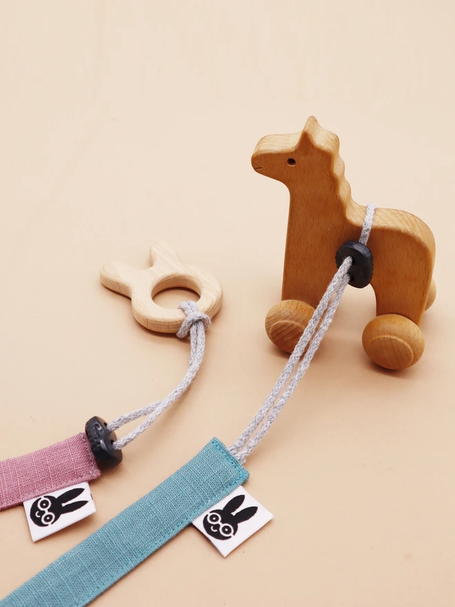 Handmade linen toy strap with grey string and a toggle attached to wooden baby toys,