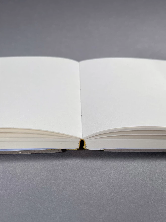 Open blank sketchbook, showcasing the flat opening of sketchbook because of fabric spine. On a light grey studio background.