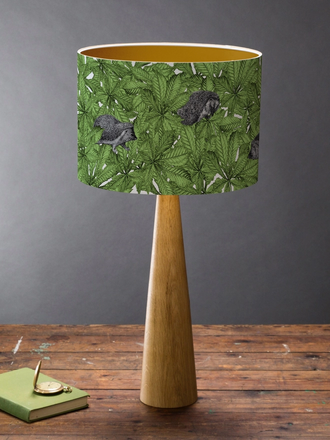 Drum Lampshade featuring hedgehogs in green leaves on a wooden base on a shelf with books and ornaments