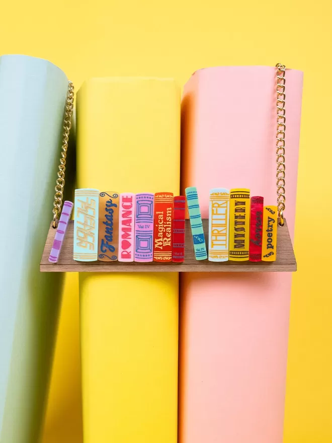 A Tatty Devine World book day bookshelf necklace hanging on some books arranged on a colourful background,