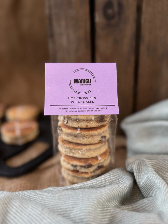 6 Hot Cross bun Welsh Cakes in a Pack with a light purple MamGu Welshcakes label on top with a rustic kitchen behind