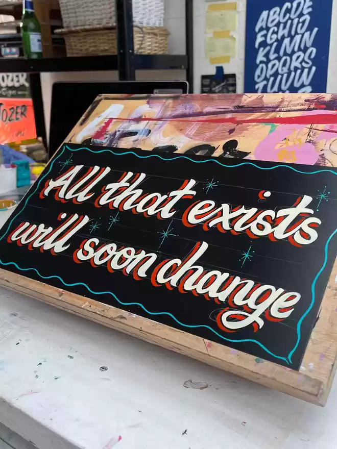 'All that exists will soon change' on a black background with ivory lettering, red drop shade and turquoise border and stars.