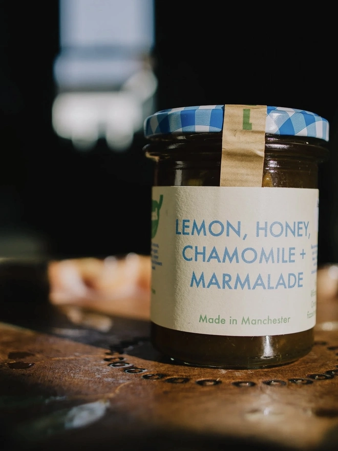 Lemon, Honey & Chamomile Marmalade Jar, jar of marmalade with a blue lid on a decorated plate, on a table. 