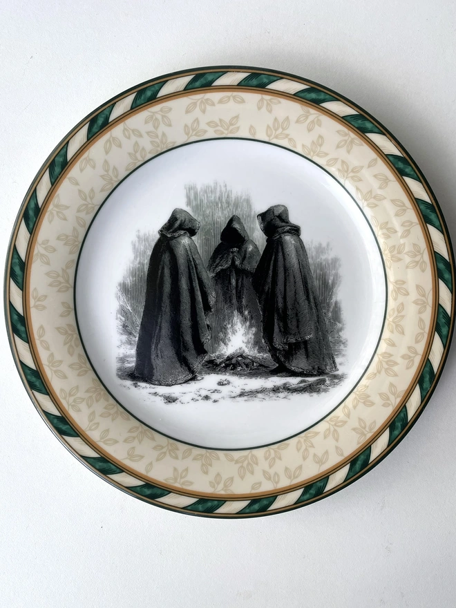 vintage plate with an ornate border, with a printed vintage illustration of hooded traitor figures in the middle