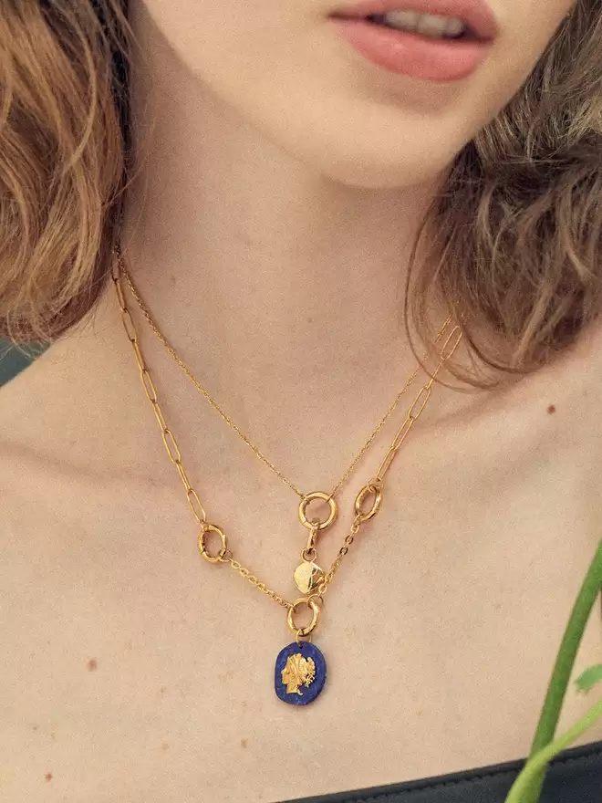 woman wearing two gold necklaces styled with a monogram engraved charm and a lapis lazuli Aphrodite medallion