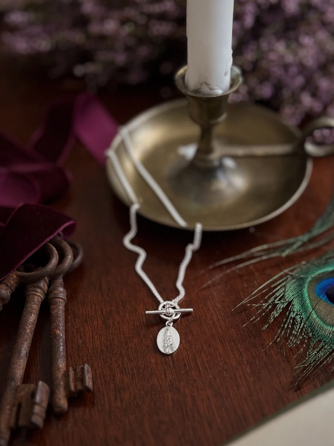 Sterling silver t - bar toggle necklace with a fern medal charm with lifestyle props including a candle and vintage keys