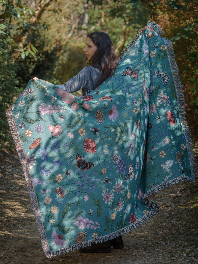 Woman wearing the 'Pollination Bloom' Recycled Cotton Blanket walking through the woods.